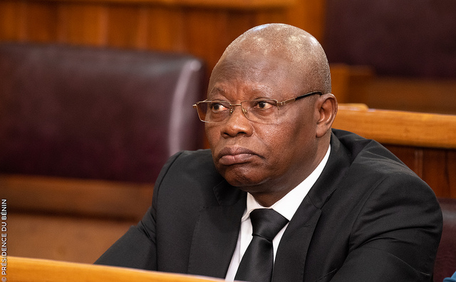 Un homme en costume sombre et lunettes assis dans une salle avec des sièges en cuir marron