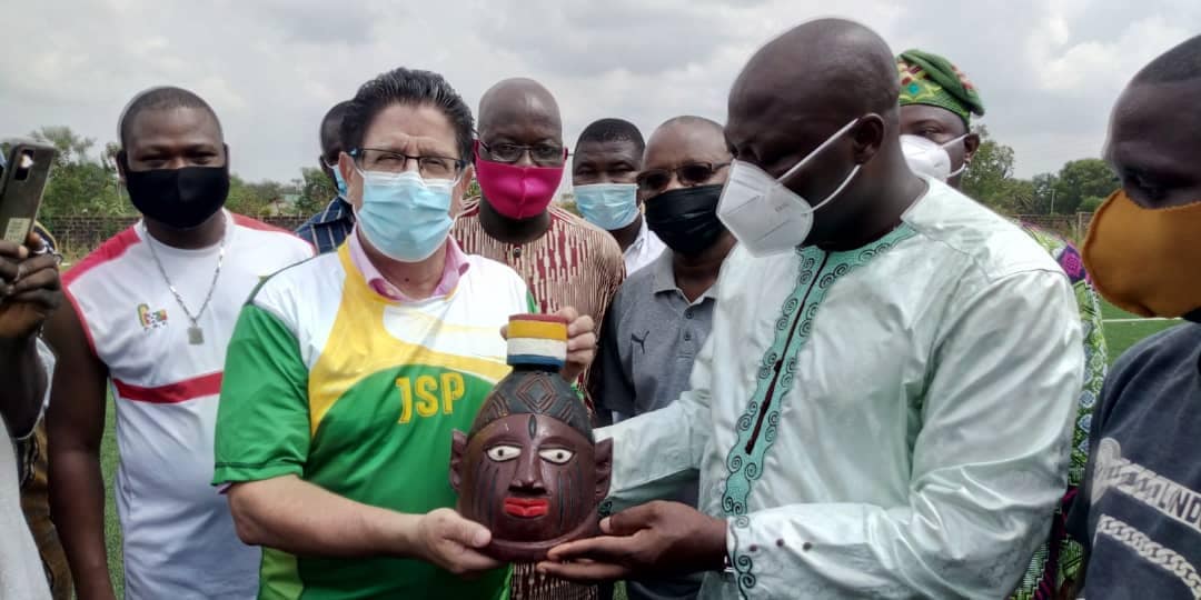 Un groupe d'hommes portant des masques de protection présente un objet artisanal en bois allongé à la forme d'une tête avec un chapeau coloré.