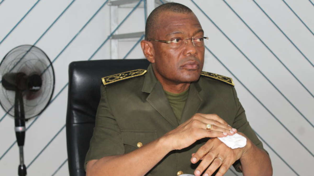 Un homme en uniforme militaire assis, regardant à droite, essuie sa main avec un mouchoir blanc