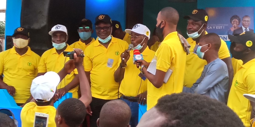 Plusieurs hommes en polo jaune et casquette, certains masqués, s’adressent à un petit groupe au cours d’un rassemblement public