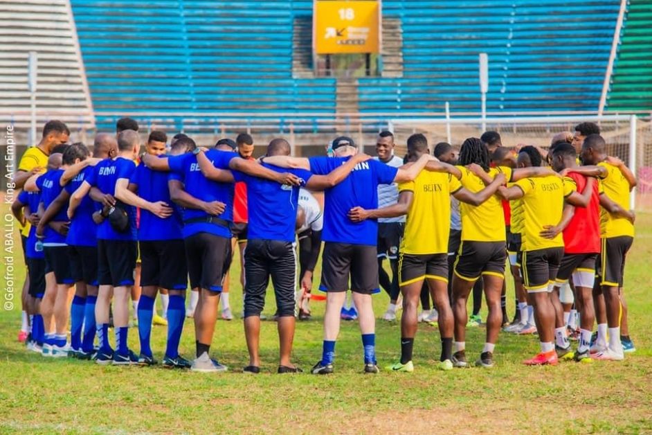 Deux équipes de football en cercle sur un terrain, bras autour des épaules lors d’une réunion collective avant un match