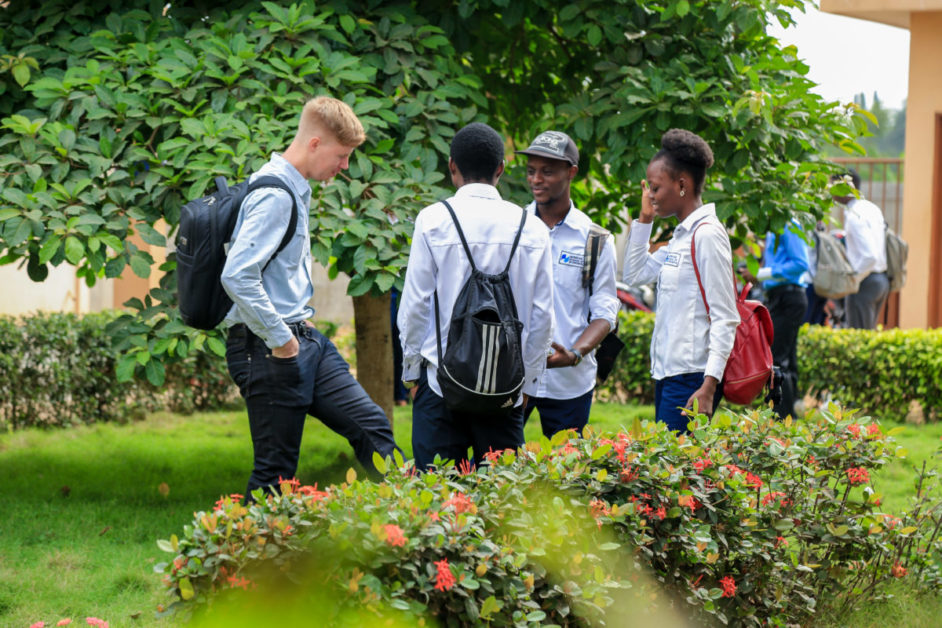 Quatre jeunes debout dans un jardin discutent près de buissons fleuris et d'arbres verts en arrière-plan