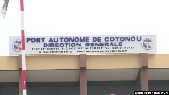 Panneau du Port Autonome de Cotonou avec coordonnées affichées sur un bâtiment beige et poteau rouge et blanc devant