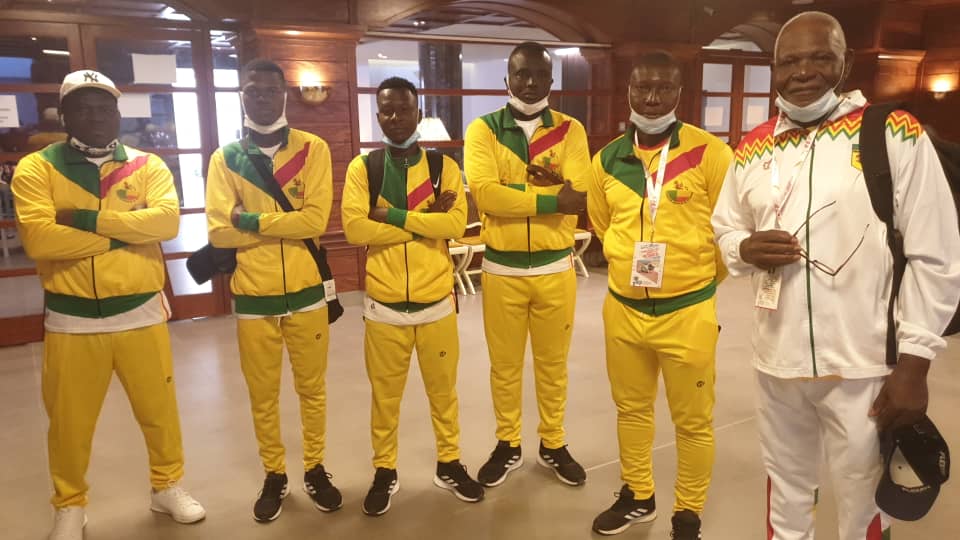 Six hommes portant des survêtements jaunes et un homme en tenue blanche posent dans un intérieur lumineux