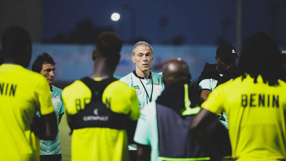 Un homme au centre parle à un groupe de joueurs en maillot jaune marqué BENIN lors d’un entraînement en soirée