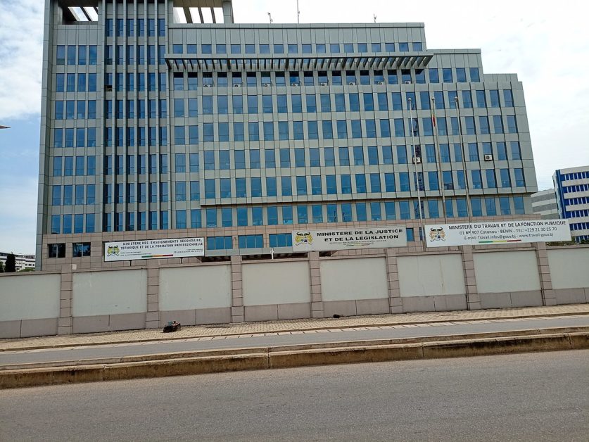 Façade d un grand bâtiment administratif avec plusieurs panneaux indiquant des ministères devant un trottoir et une route