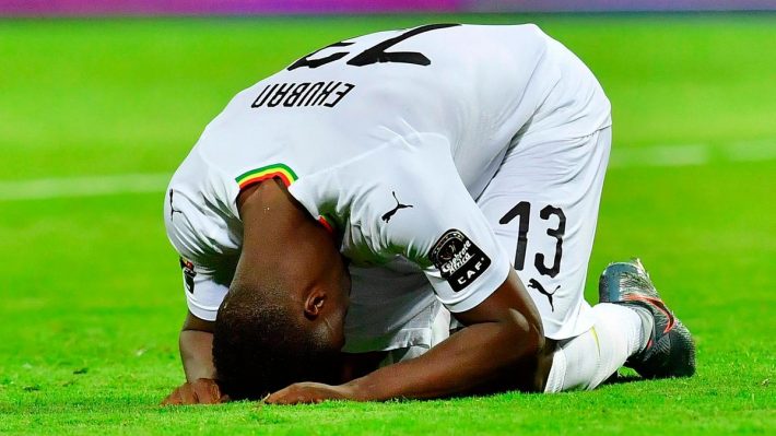 Un joueur de football agenouillé tête baissée sur le gazon vert en signe de déception ou de frustration
