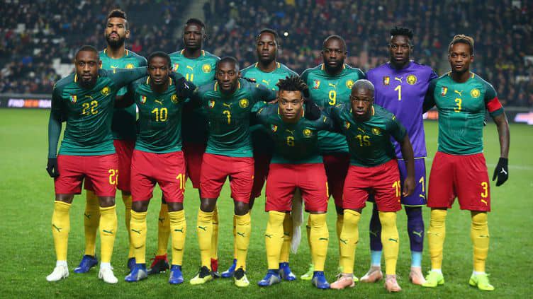 Onze joueurs de football en tenue verte, rouge et jaune posant ensemble sur un terrain avec un public en arrière-plan
