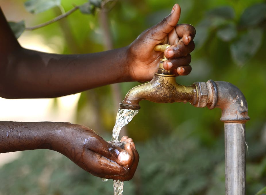 Des mains recueillent de l’eau qui coule d’un robinet en extérieur dans un environnement naturel vert