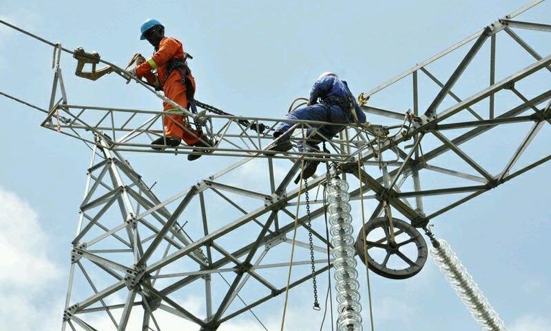 Deux ouvriers en tenue de sécurité travaillent en hauteur sur une structure métallique de ligne électrique sous un ciel bleu