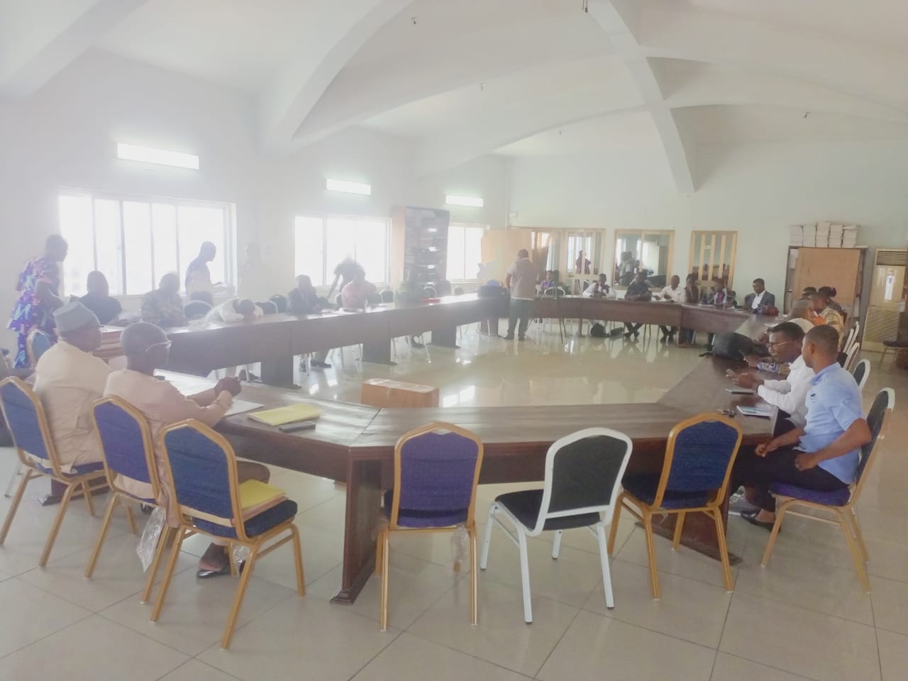 Personnes assises en réunion autour d'une grande table en U dans une salle lumineuse avec plafond voûté