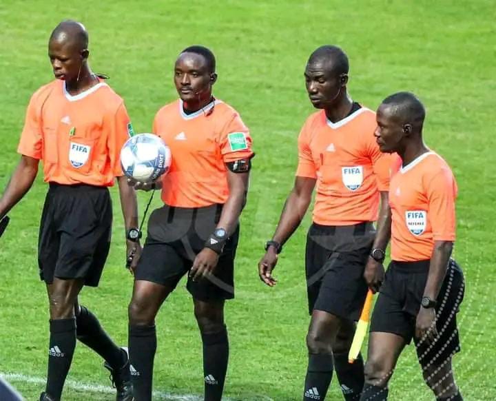 Quatre arbitres en tenue orange et noire marchent sur le terrain de football pendant un match