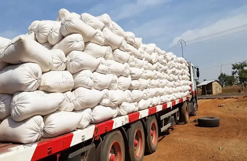 Camion chargé de sacs blancs empilés sur une route poussiéreuse sous un ciel bleu partiellement nuageux