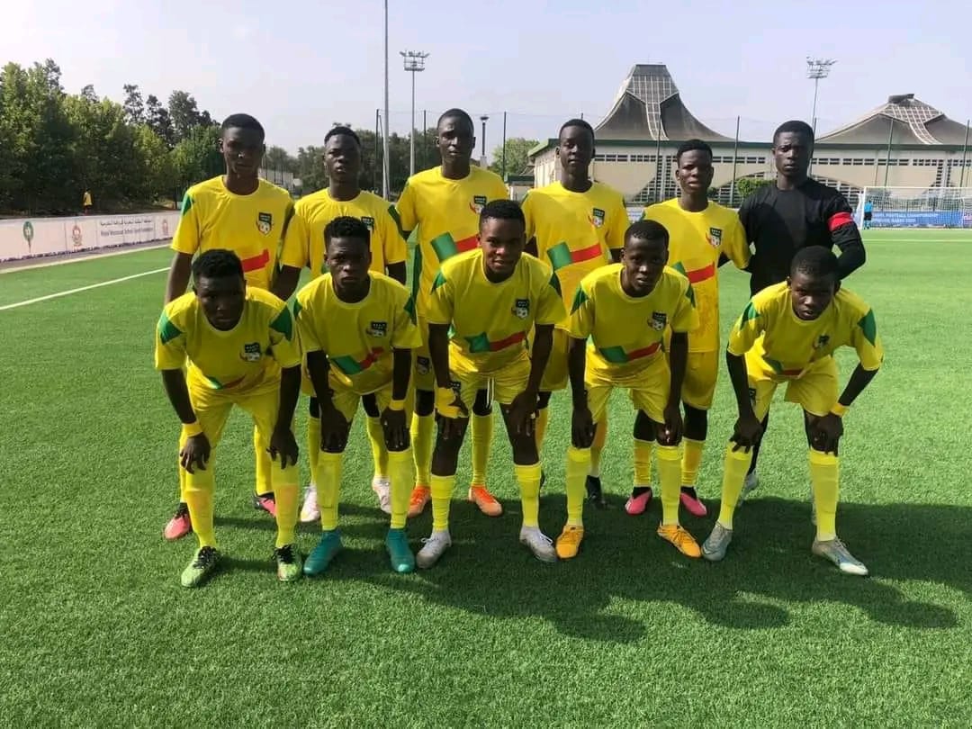 Dix jeunes joueurs de football en tenue jaune posent sur un terrain vert devant un stade moderne par temps clair