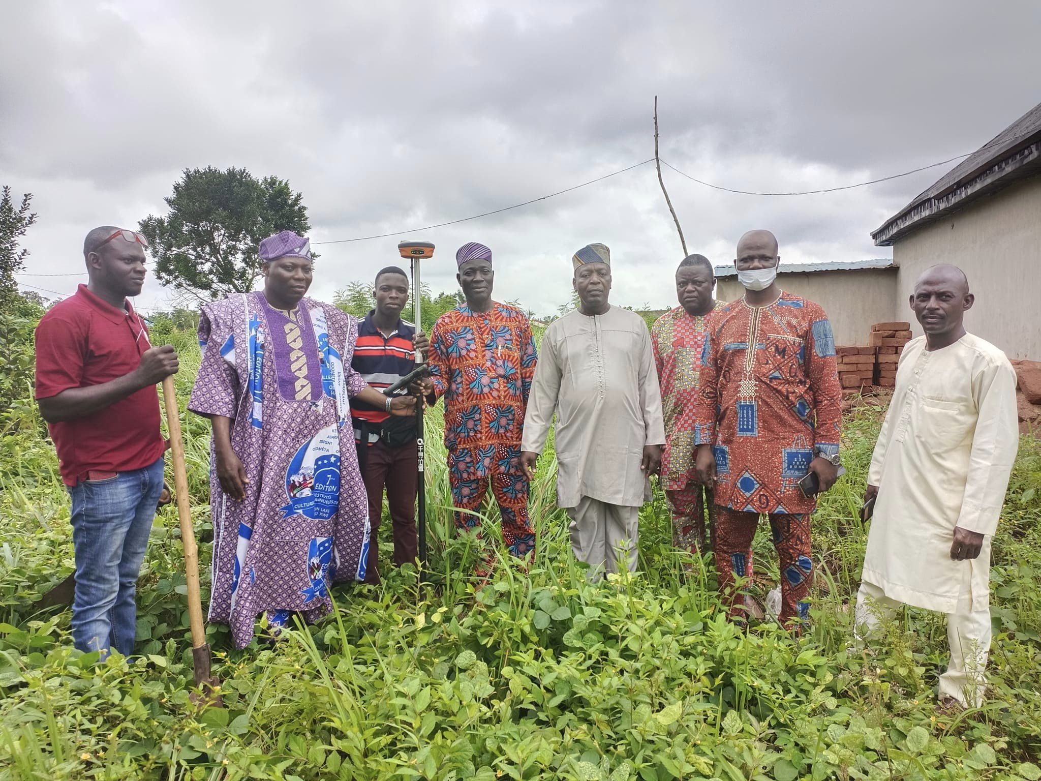 Un groupe d'hommes vêtus de tenues traditionnelles et modernes posent dans un terrain verdoyant sous un ciel nuageux