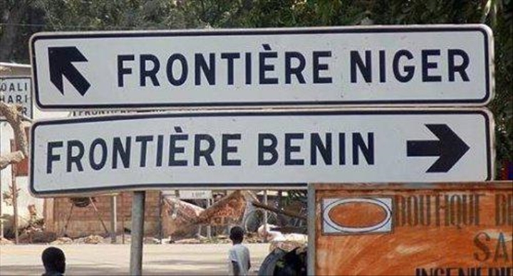 Panneaux de signalisation indiquant la direction des frontières Niger et Bénin avec des passants en arrière-plan