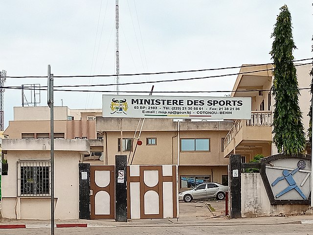 Entrée d'un bâtiment avec un panneau indiquant Ministère des Sports et des coordonnées affichées au-dessus du portail
