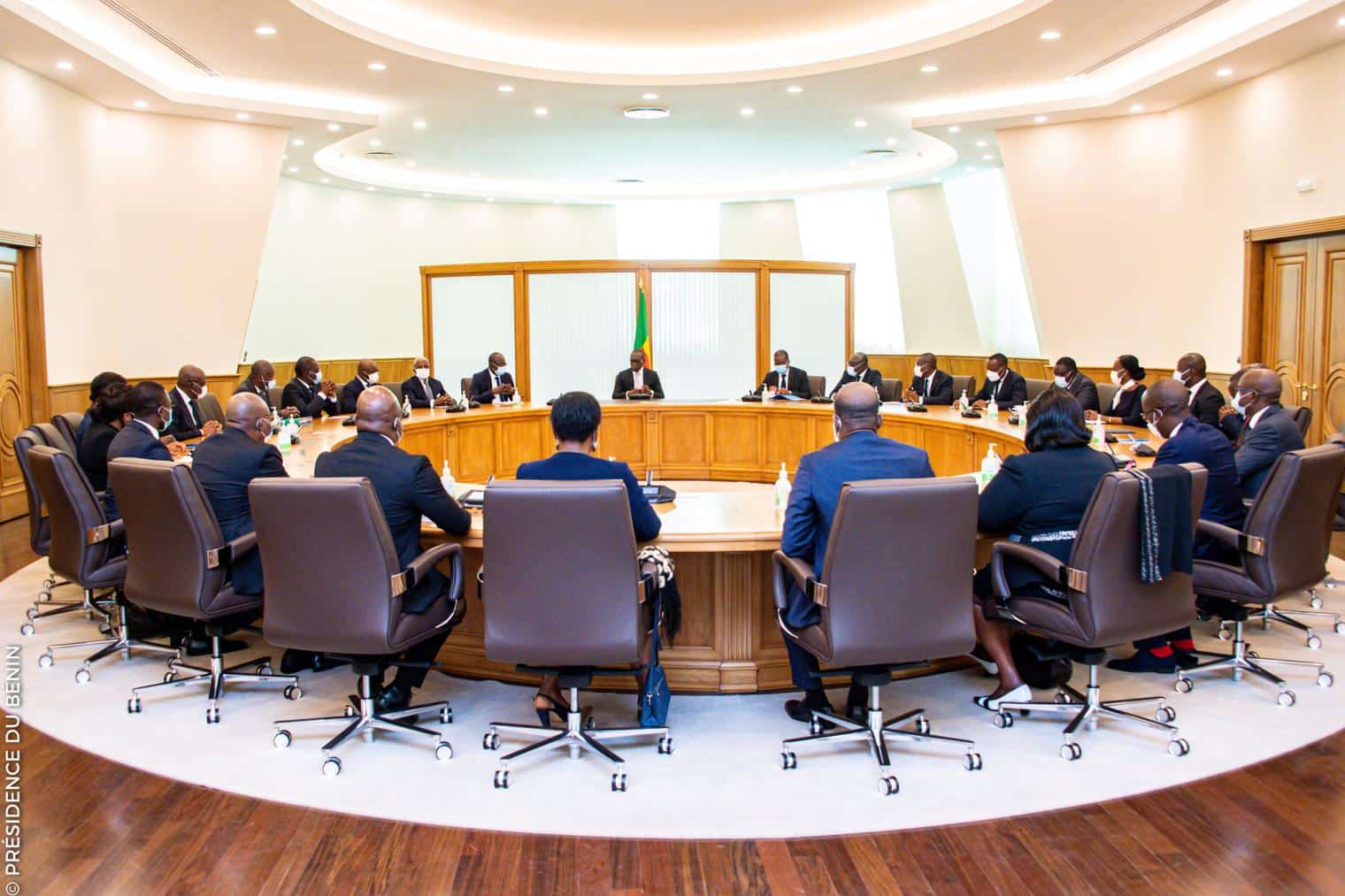Personnes en costume assises autour d'une grande table ronde dans une salle lumineuse avec un drapeau au centre du mur arrière