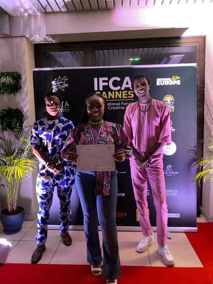 Trois personnes souriantes posent sur un tapis rouge devant un panneau IFCA Cannes dont une tient un certificat