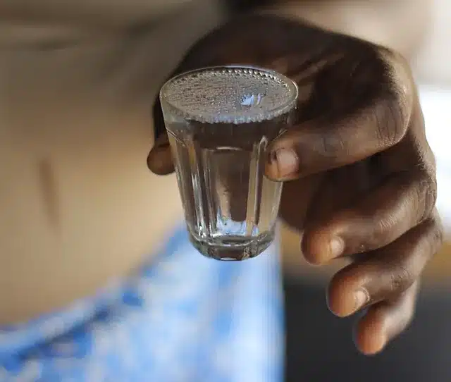 Une main tenant un petit verre transparent rempli d un liquide clair