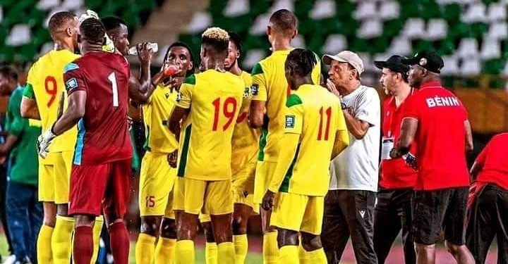 Des joueurs de football en maillot jaune et rouge sont regroupés sur le terrain pour une discussion avec des entraîneurs en tenue décontractée