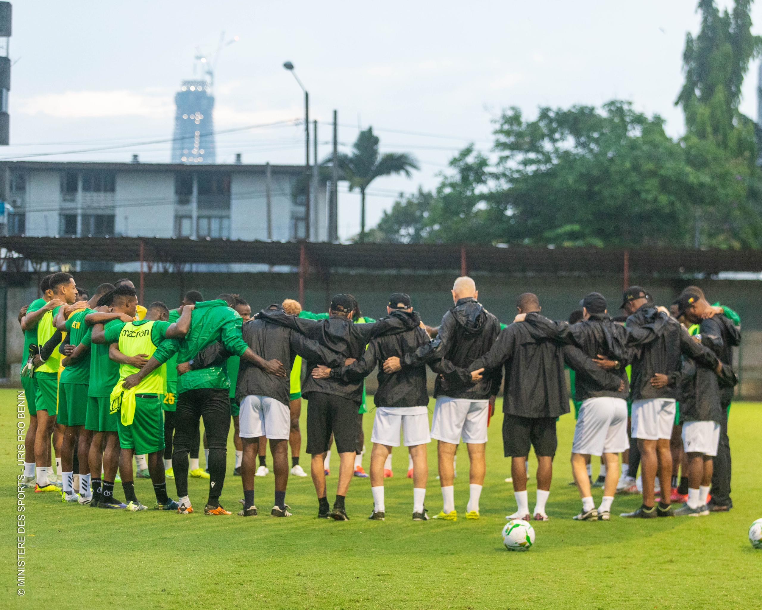 Des joueurs de football en tenue de sport forment un cercle bras dessus bras dessous sur un terrain en herbe au crépuscule
