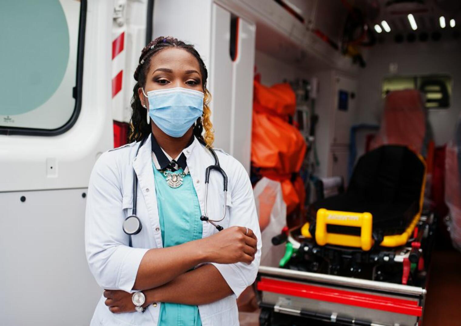 Jeune professionnelle médicale portant masque et blouse devant un brancard à l’intérieur d’un véhicule sanitaire