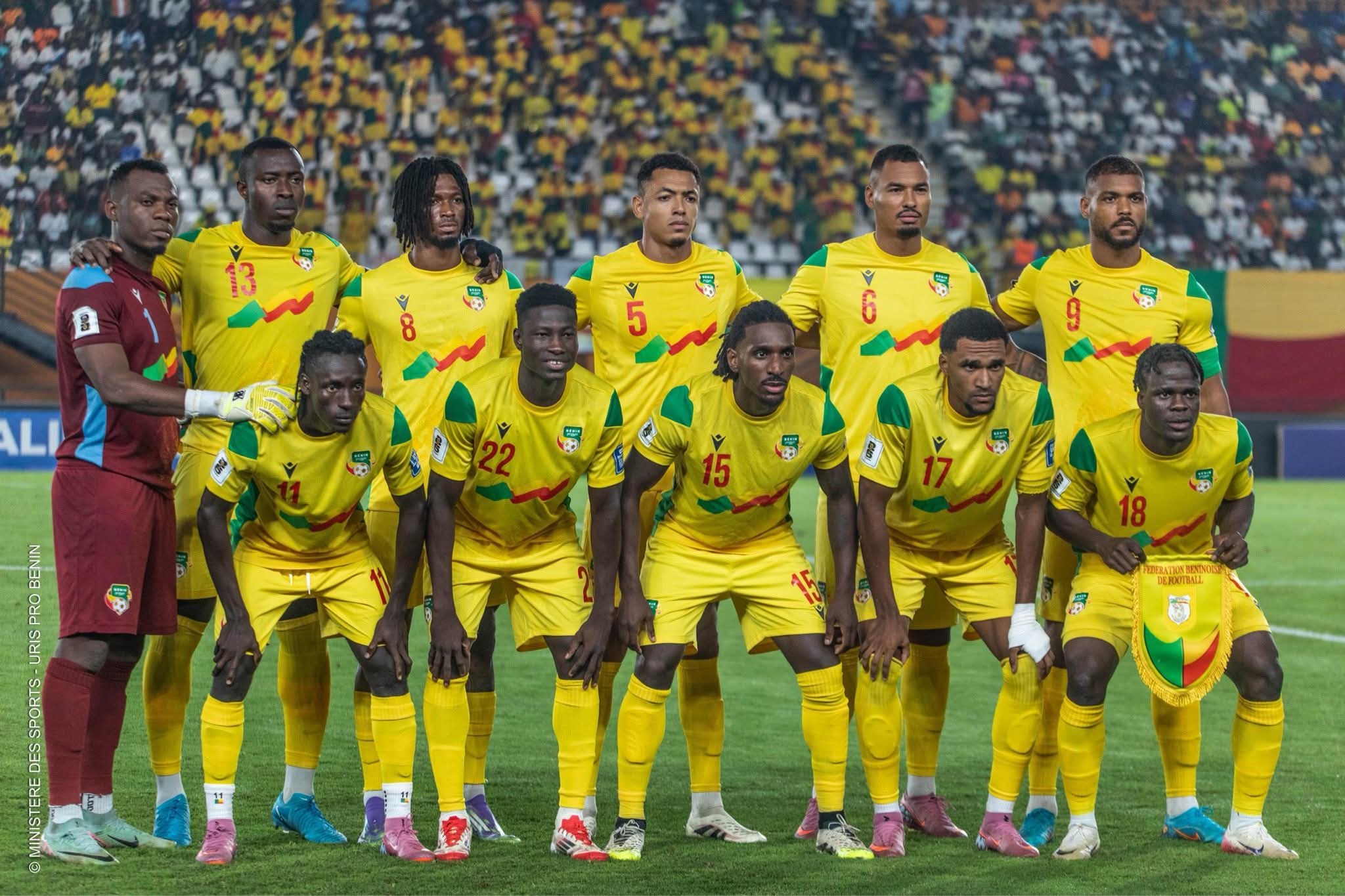 Onze joueurs de football en maillot jaune posent en rang sur un terrain devant un public nombreux dans un stade.