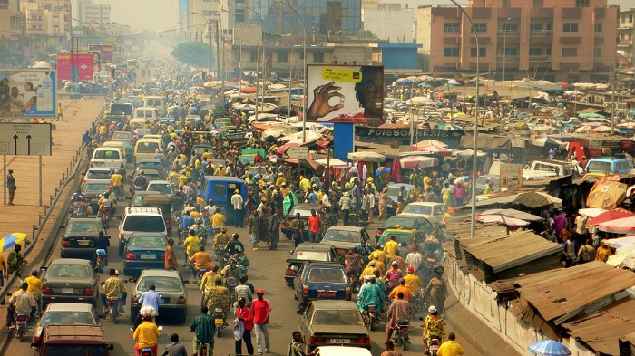 Ruelle très fréquentée avec de nombreux piétons et véhicules au milieu de bâtiments urbains dense et étals de marché sur le côté