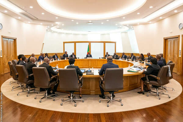 Personnes en costume assises autour d'une large table ronde dans une salle éclairée et moderne avec un drapeau au centre
