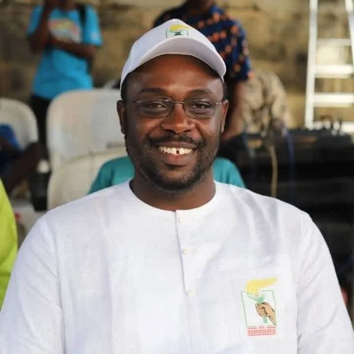 Homme souriant en chemise blanche et casquette blanche assis avec des personnes floues en arrière-plan