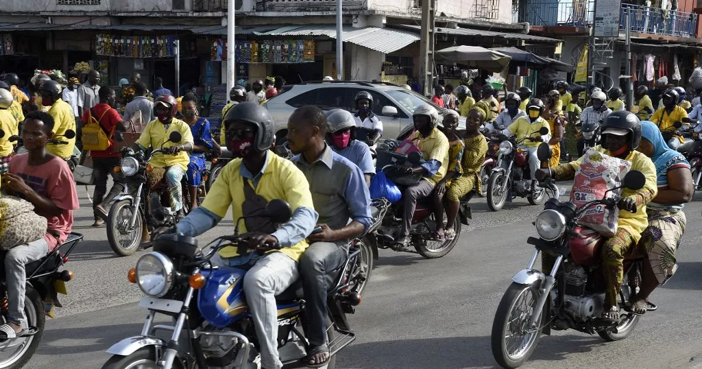 Nombreuses motos avec conducteurs portant des chemises jaunes et passagers circulant dans une rue animée d une ville africaine