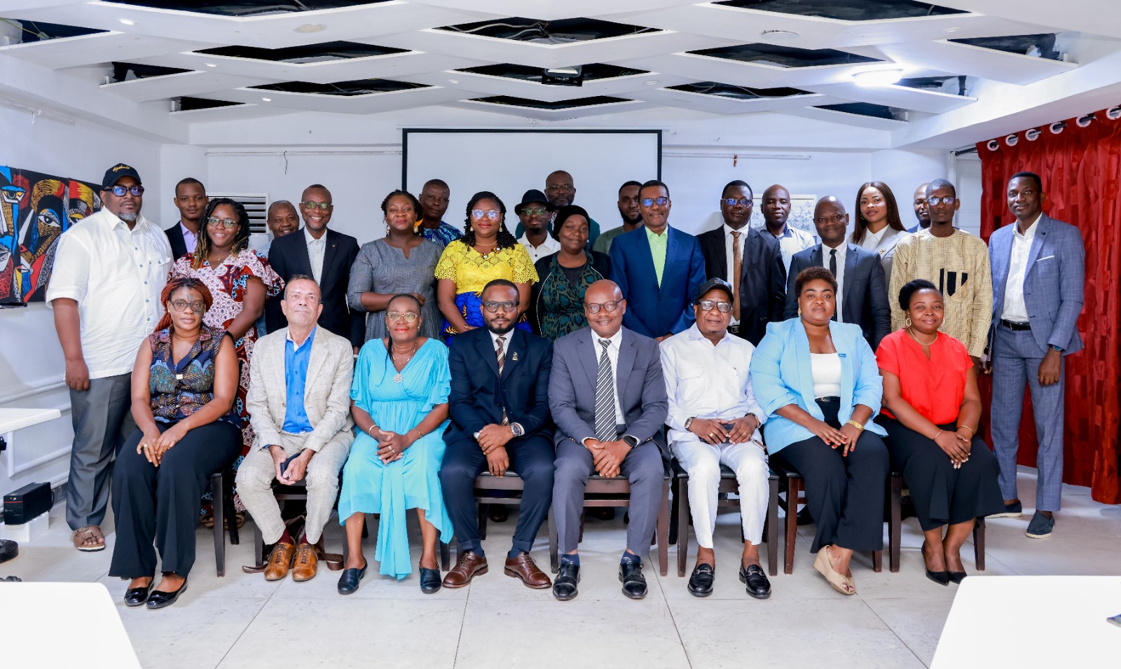 Un groupe de trente personnes posant dans une salle avec un écran derrière et des rideaux rouges sur un côté