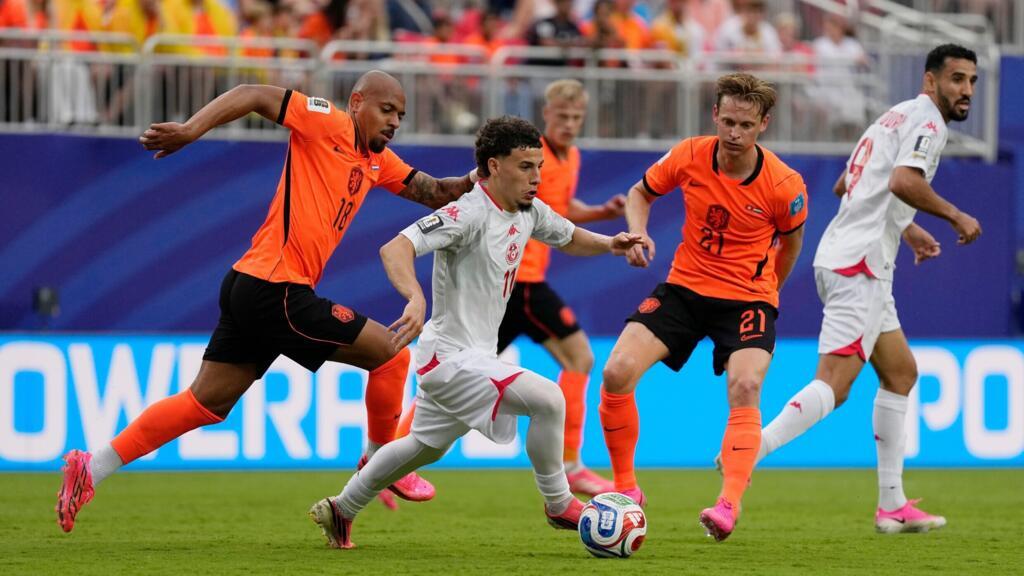 Un joueur en maillot blanc dribble un ballon sous la pression de trois joueurs en maillots orange sur un terrain de football