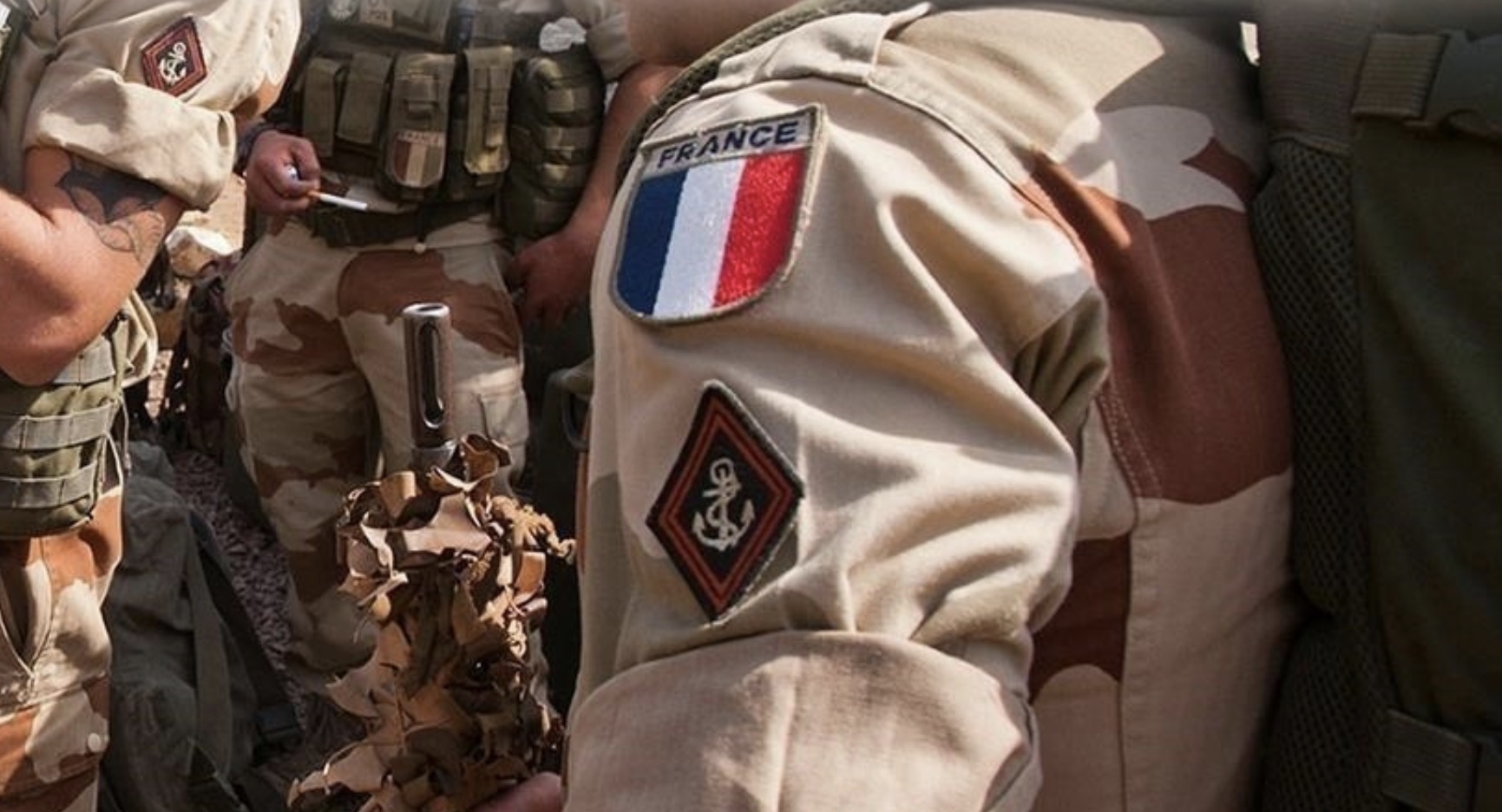 Des soldats en tenue camouflée avec un insigne tricolore français sur le bras discutent en extérieur