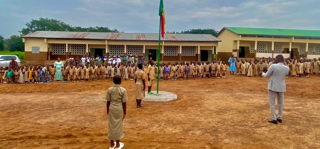 Des élèves en uniforme se tiennent en rang autour de la levée du drapeau du Bénin
